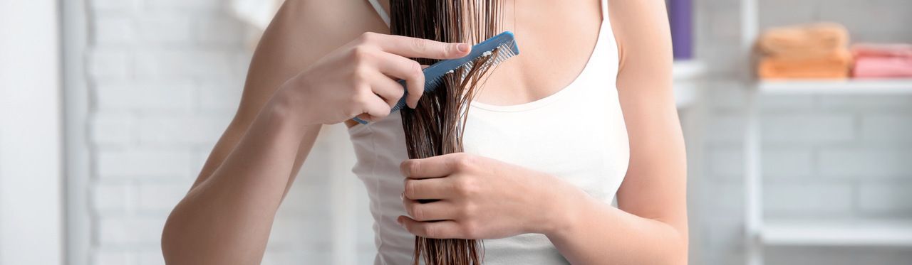 Mulher caucasiana jovem penteando o cabelo depois de aplicar queratina nos fios