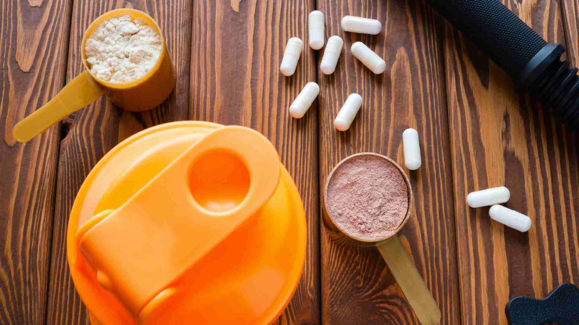 Medidor de suplemento muscular cheio de whey protein ao lado de cápsulas