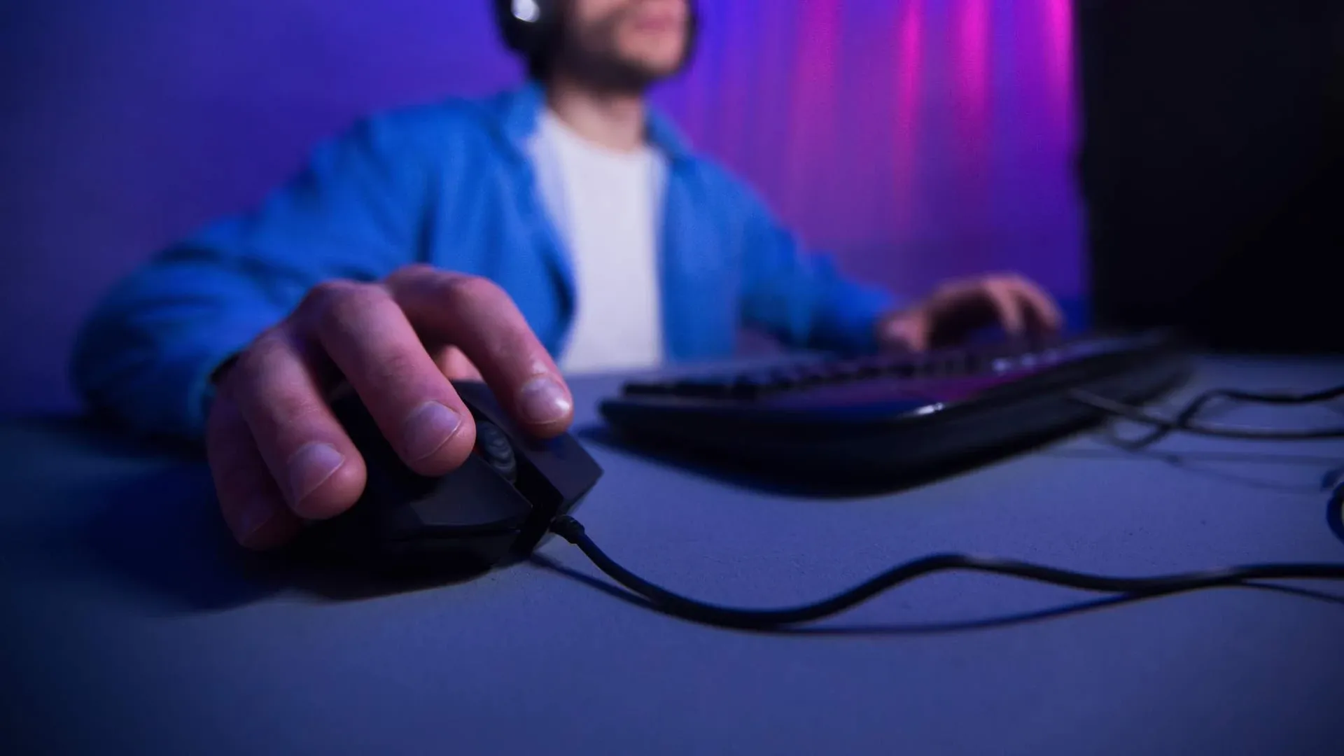 Homem branco jogando no computador, com foco em sua mão usando o mouse gamer e fundo desfocado