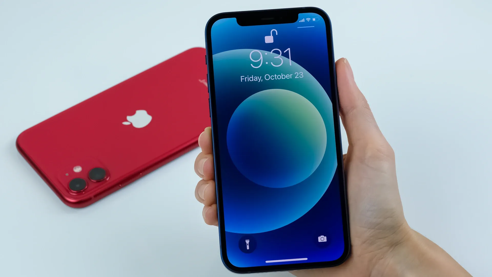 Mão segurando iPhone 12 enquanto um iPhone 11 vermelho aparece no fundo