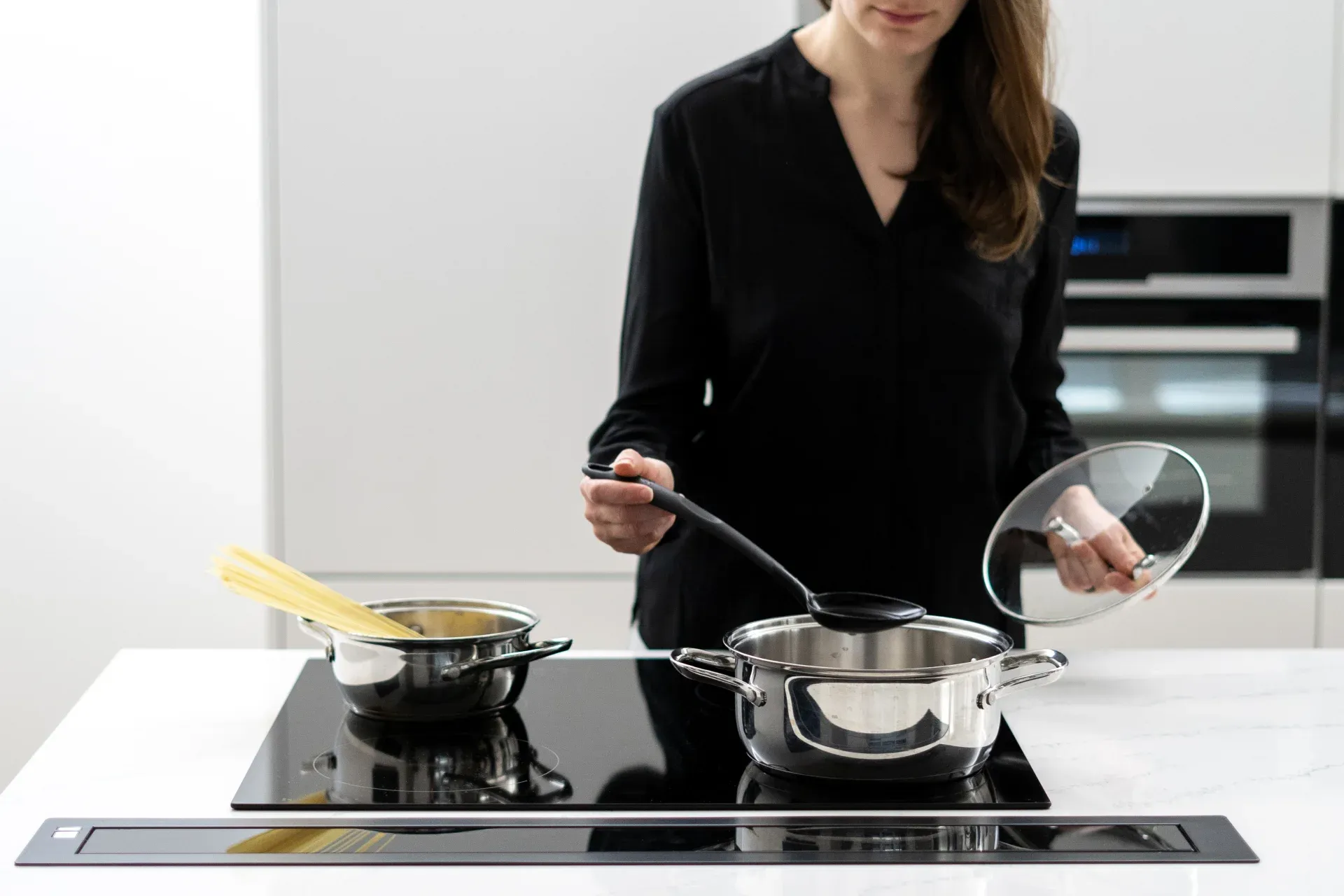 Mulher preparando comidas no cooktop de indução preto instalado em uma bancada de mármore branca