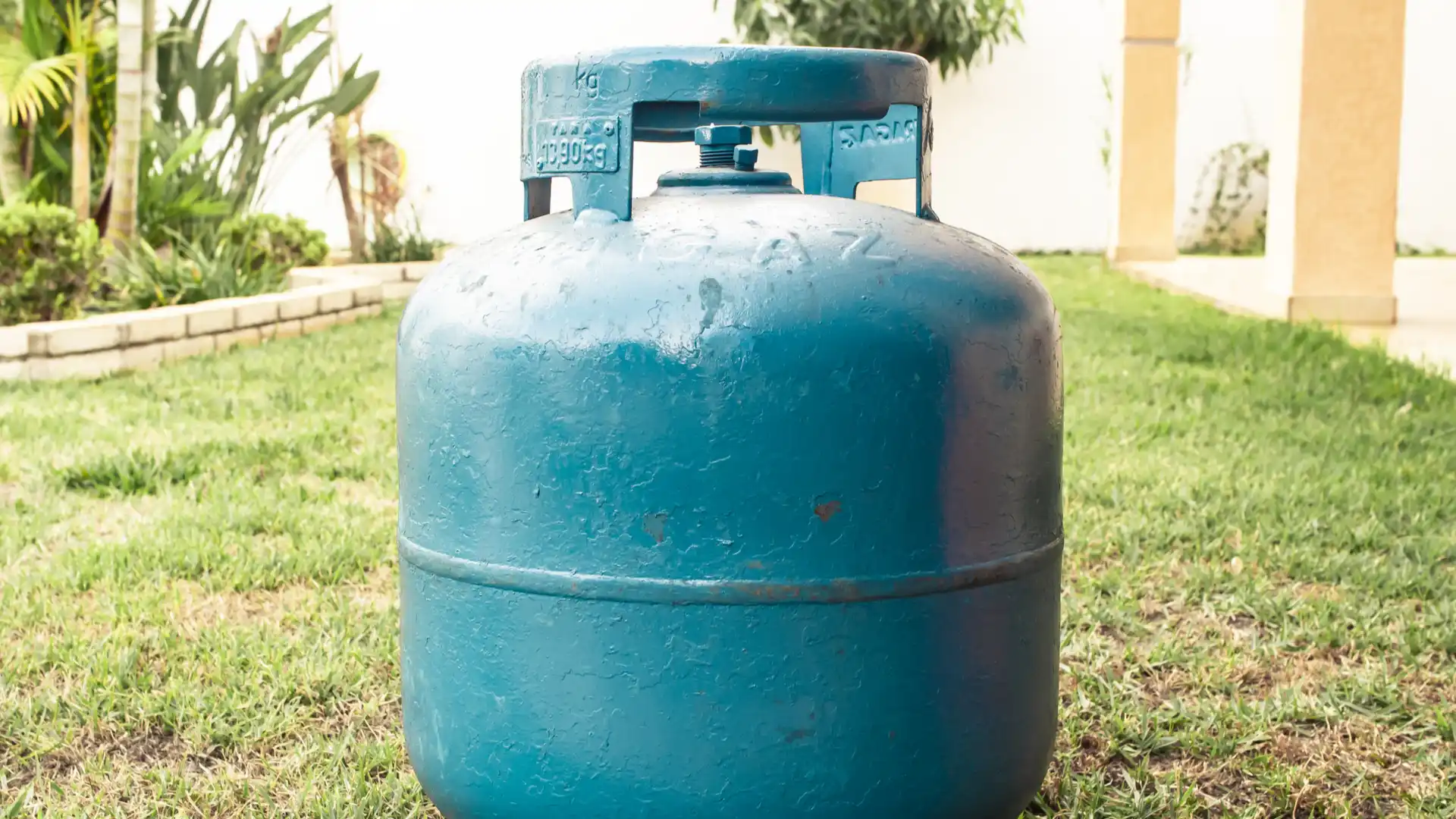Botijão de gás azul em gramado na área externa de uma casa