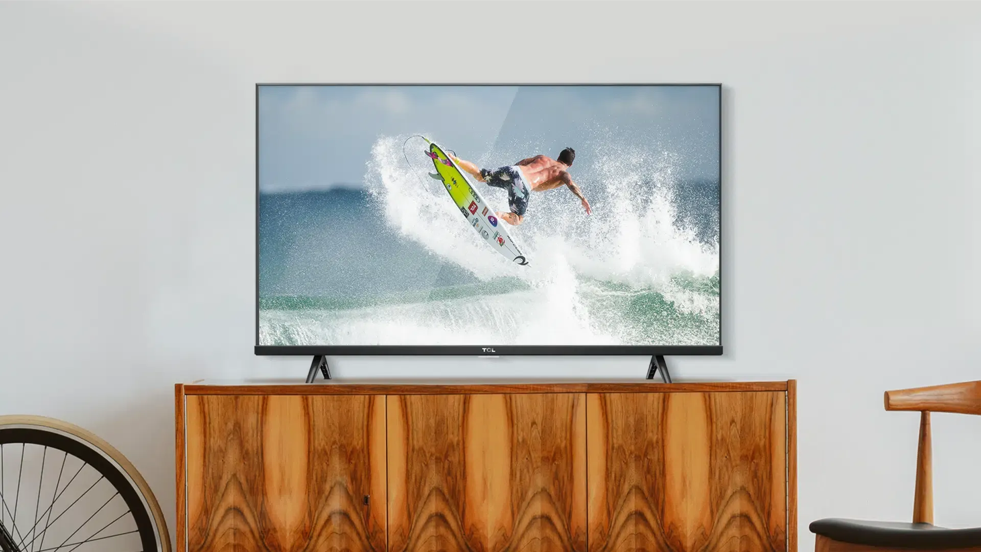 TV barata TCL S615 sobre rack de madeira, exibindo imagens de surfe.