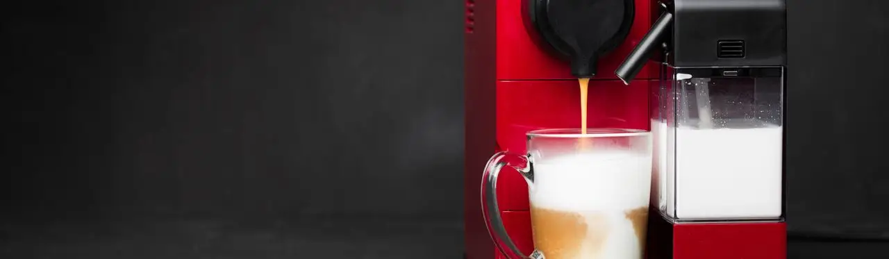 Cafeteira elétrica vermelha passando um café com leite em xícara transparente 