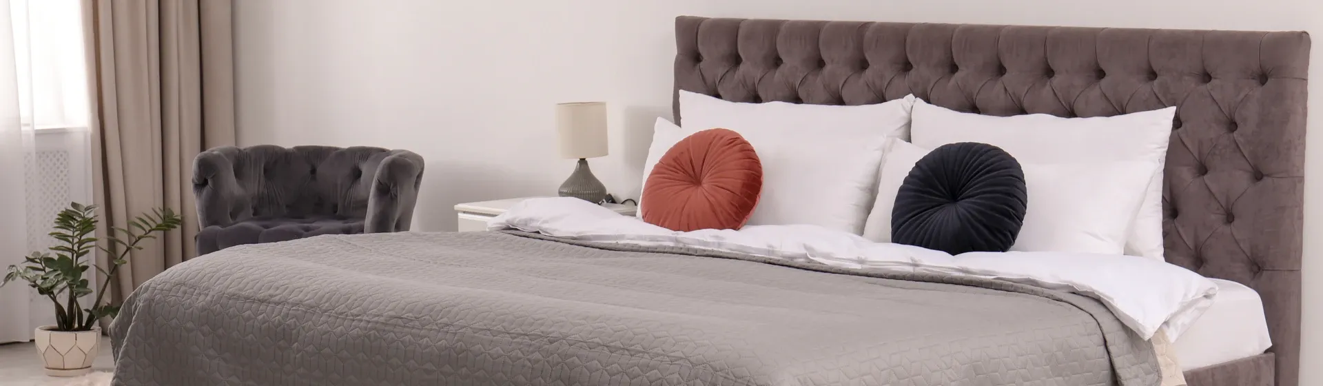 Cama de casal com cabeceira cinza, travesseiros brancos e colcha cinza em quarto