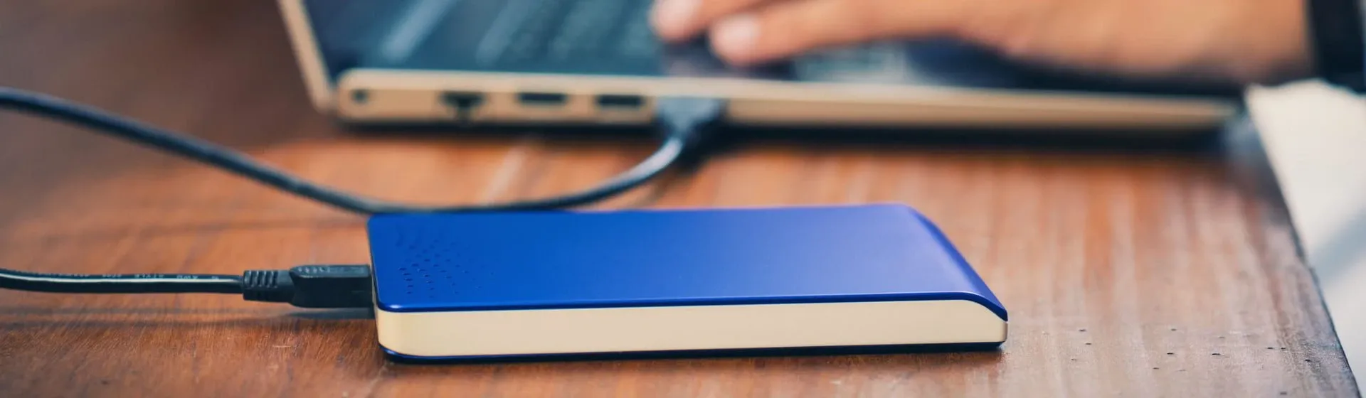 HD externo azul conectado à notebook sobre mesa de madeira