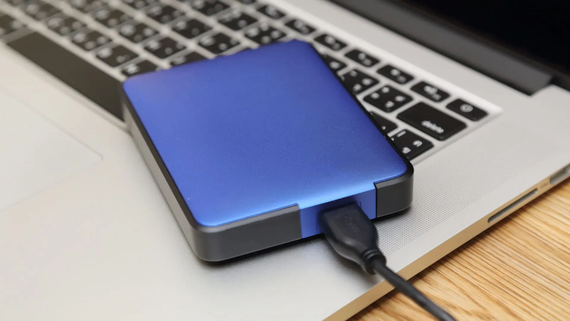 HD externo azul conectado por USB e em cima de notebook prata