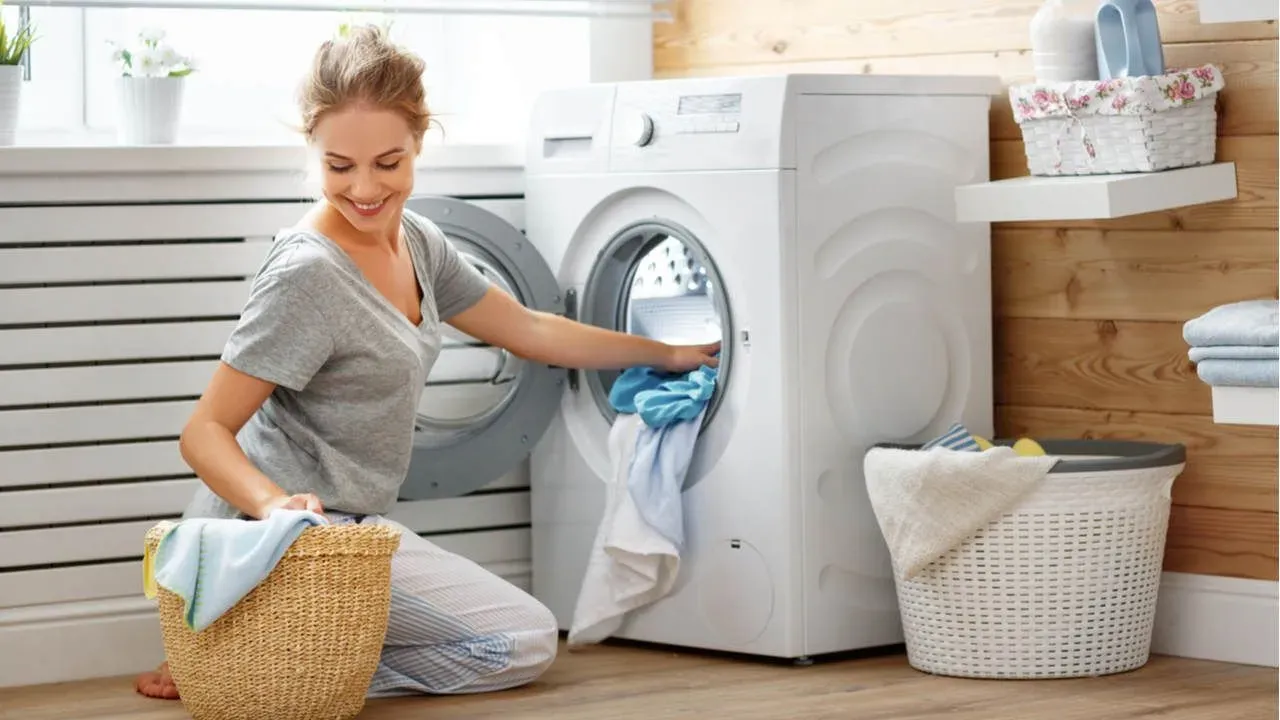 Mulher branca jovem sorrindo e colocando roupas para lavar em lavadora front load