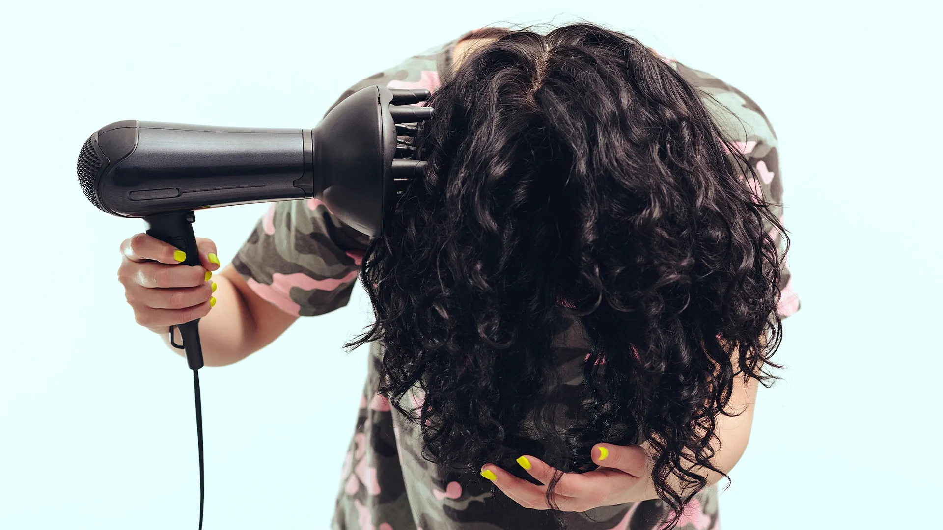 Mulher secando os cabelos com o auxílio de um difusor 