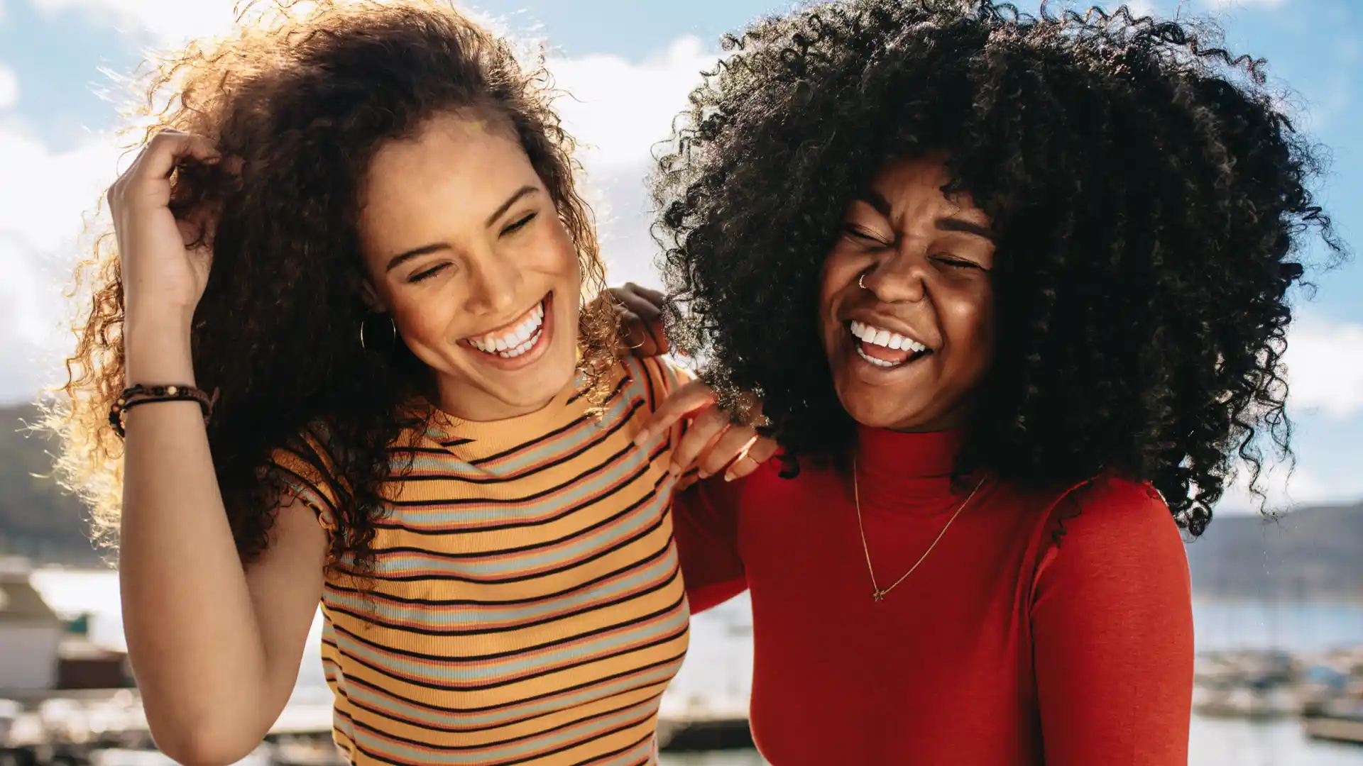 Duas mulheres negras sorrindo com seus cachos soltos