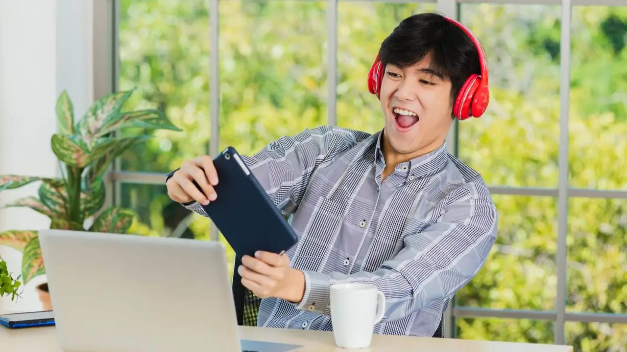 Homem joga em tablet para jogos usando headphone vermelho