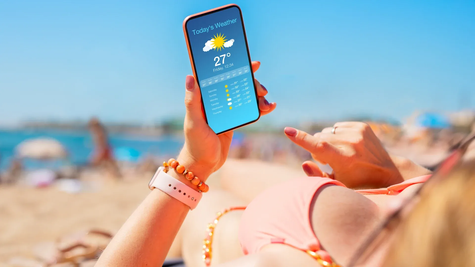 Mulher usa celular na praia, sob o sol