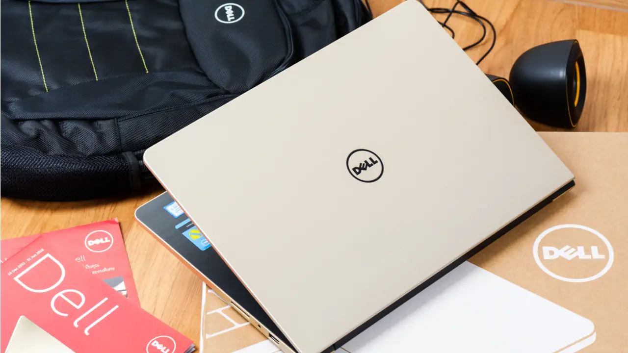 Notebook Dell branco em cima de uma mesa ao lado de mochila, caixa e panfletos da marca