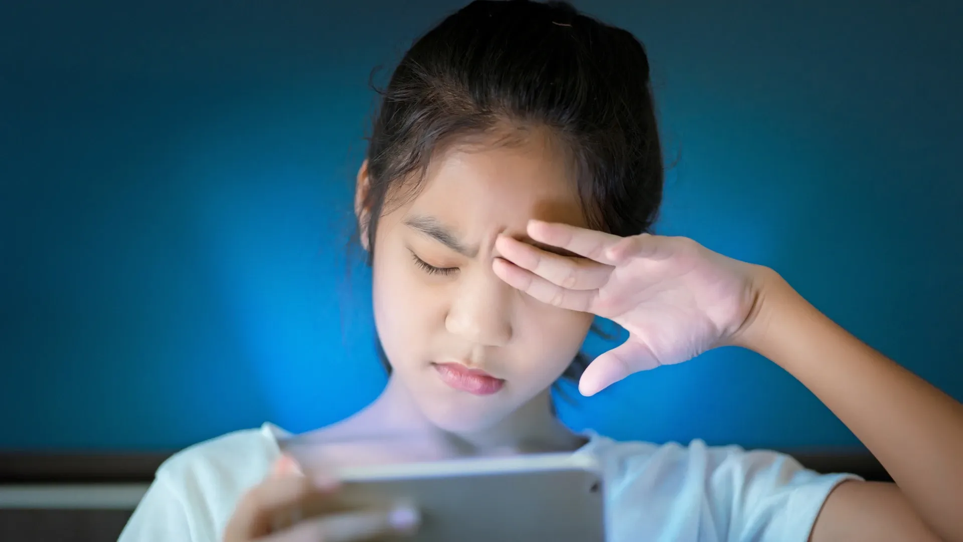 Menina coçando os olhos enquanto segura o celular
