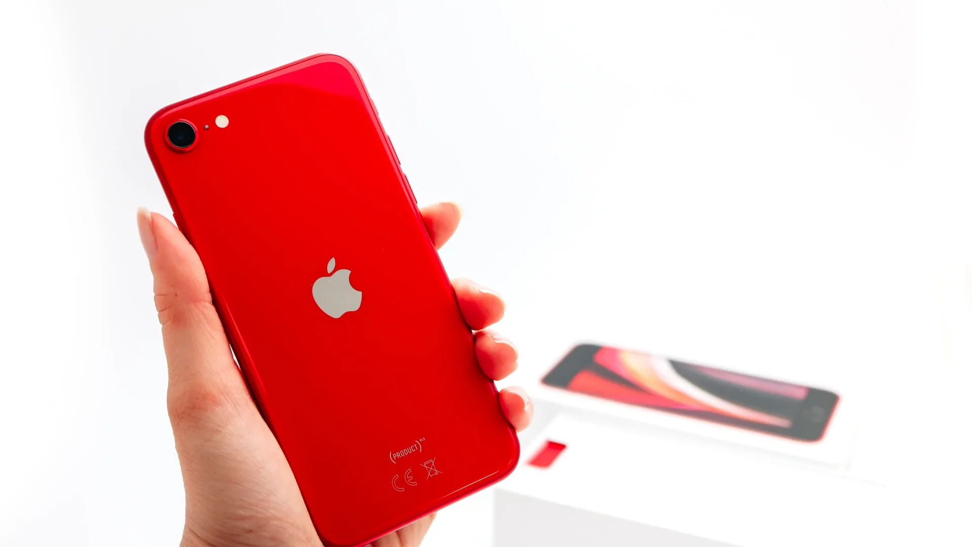 Foto de uma pessoa segurando o iPhone SE 2020 na cor vermelha com fundo branco