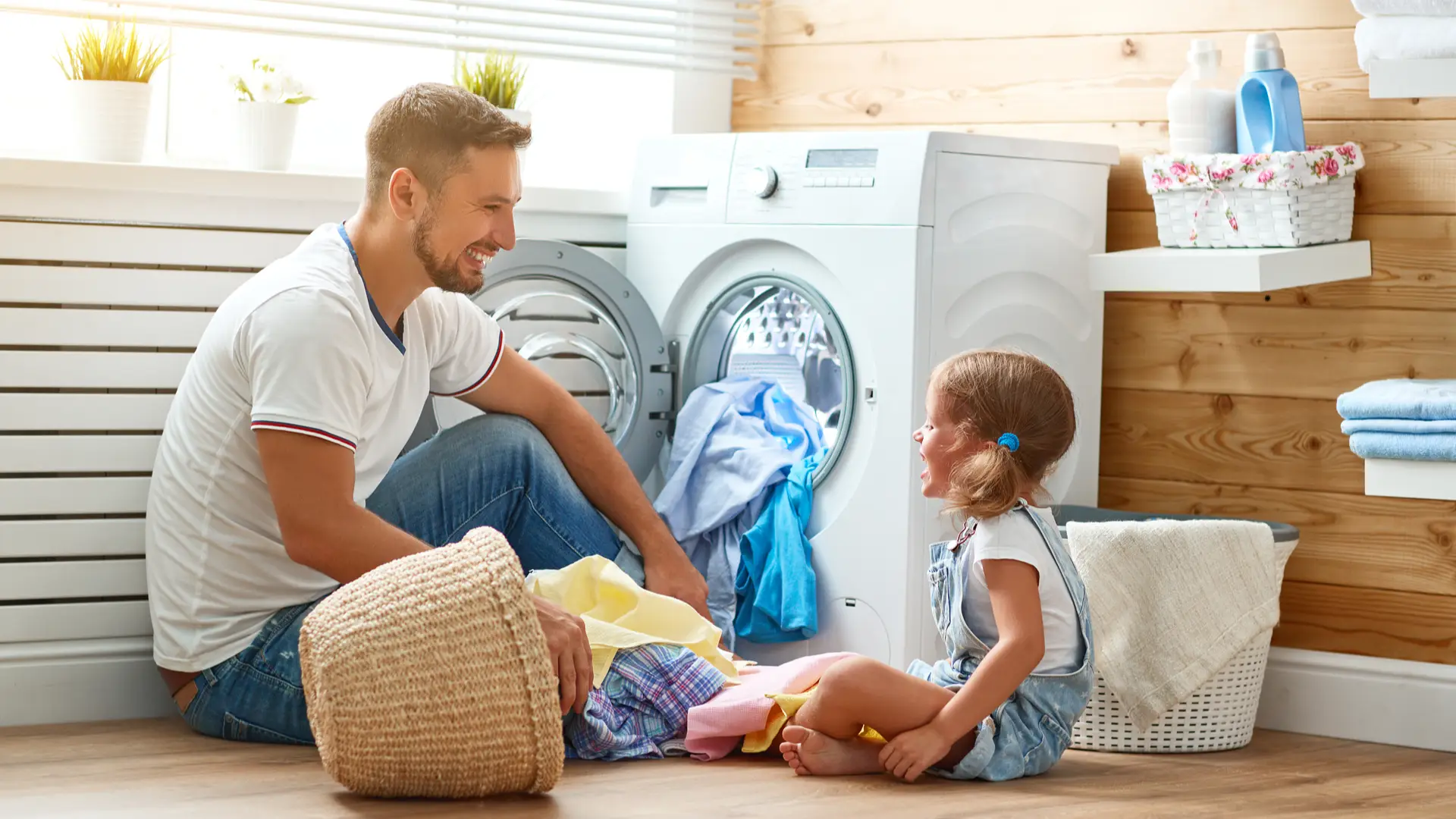 Pai e filha recolhem a roupa seca de uma lavadora frontal