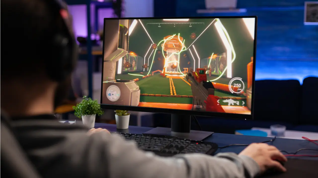 Homem jogando um jogo de tiro em um monitor gamer barato, enquanto usa outros equipamentos, como teclado, headphone e mouse