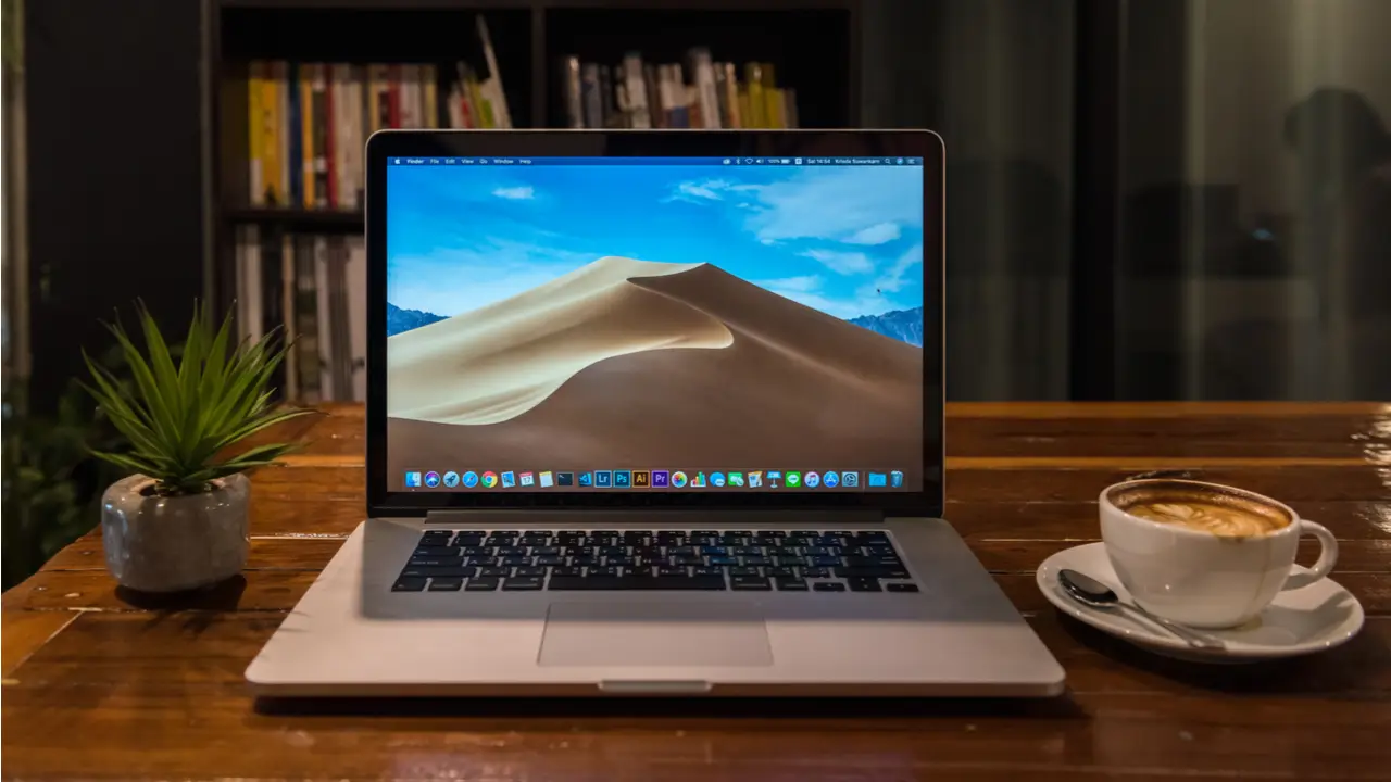 MacBook em mesa de madeira ao lado de xícara de café