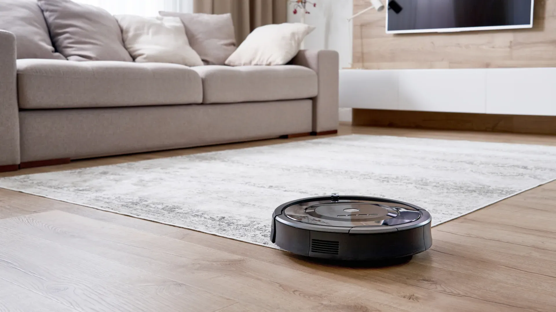 Aspirador robô barato preto passando por cima de tapete em sala de estar