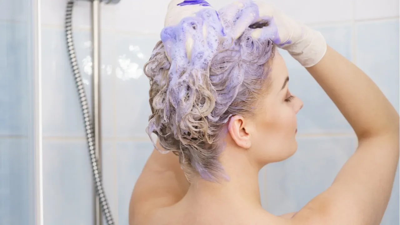 Mulher no banho lavando o cabelo platinado com shampoo roxo