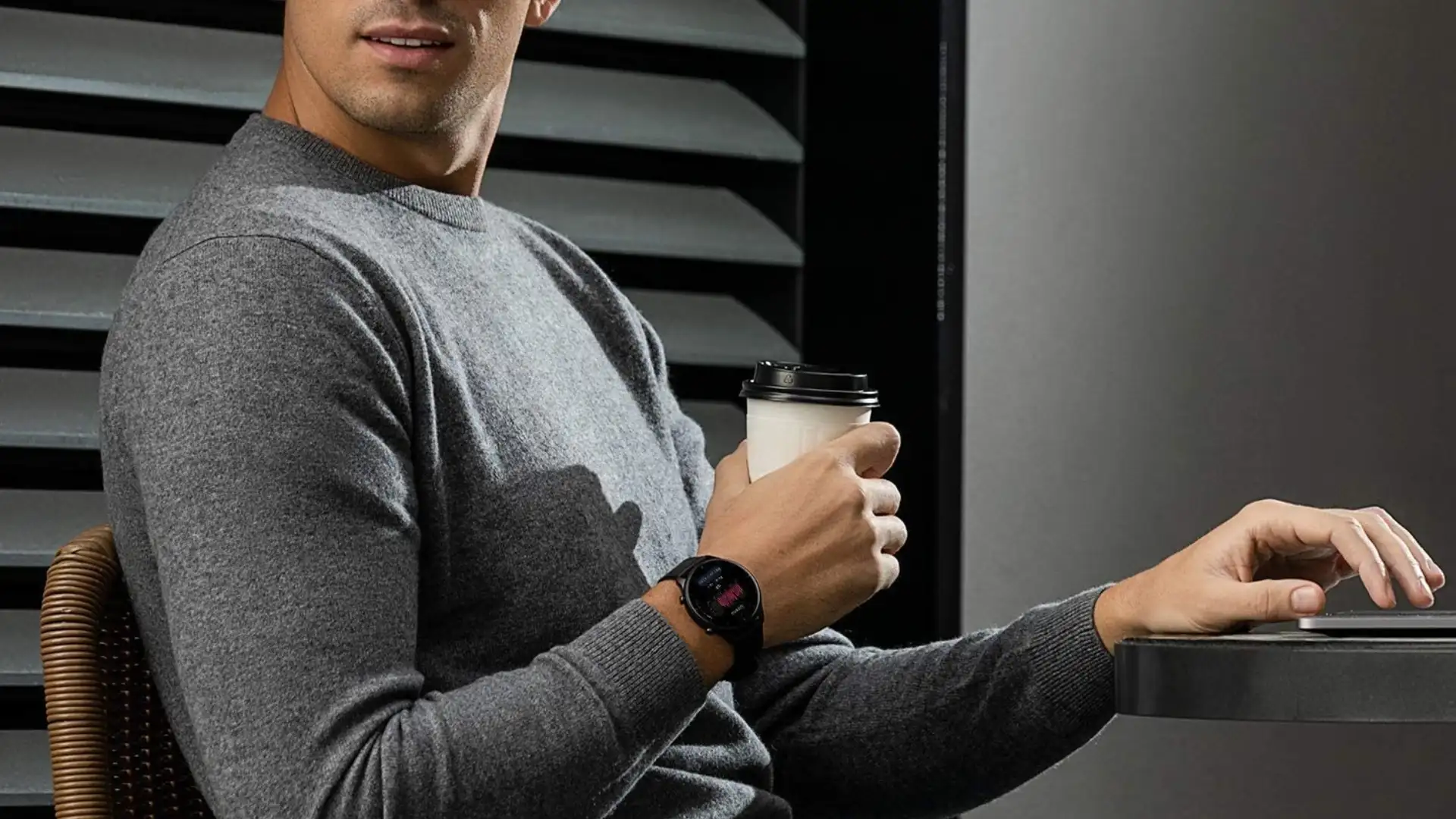Homem branco usa smartwatch redondo masculino Amazfit GTR 2e enquanto segura um copo de café e usa o computador