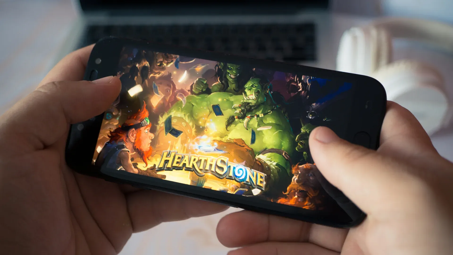 Mãos segurando celular com o jogo Hearthstone na tela