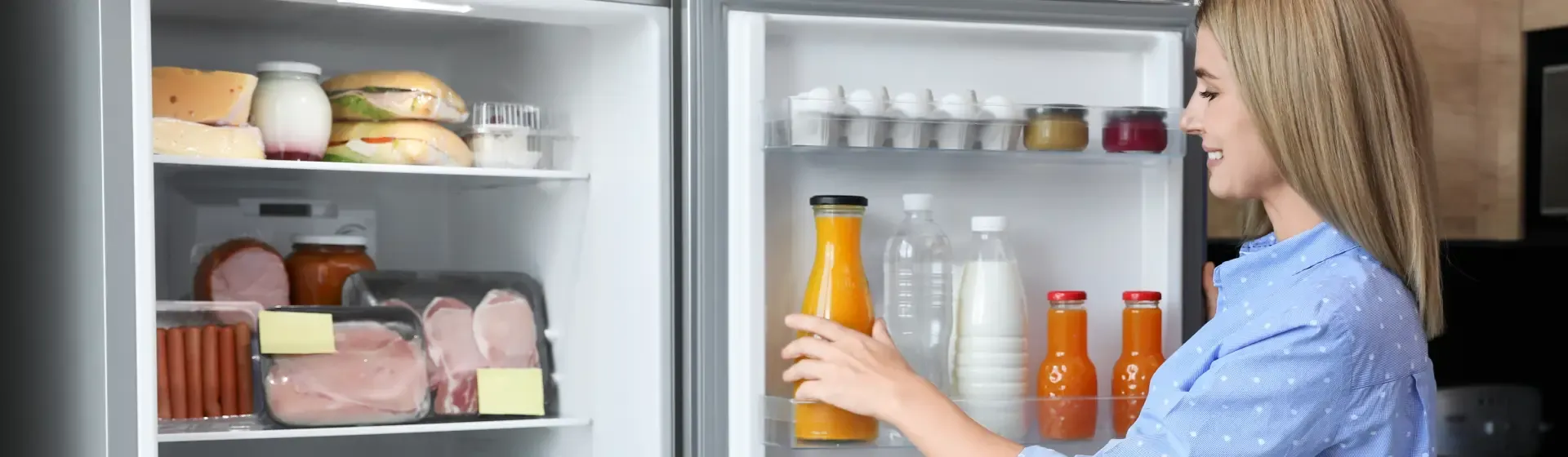 Mulher mexendo na geladeira aberta com frios e suco de laranja