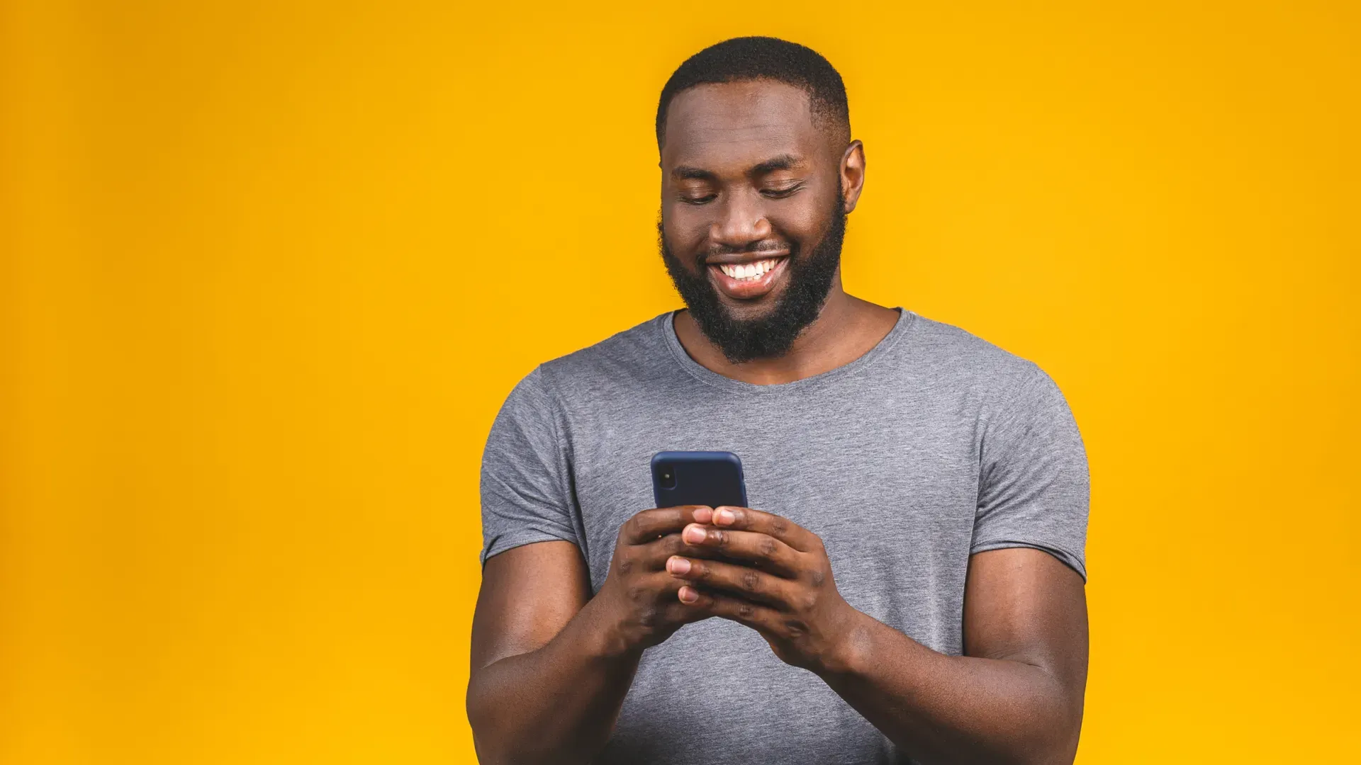 Homem de camisa cinza em fundo laranja usa celular azul