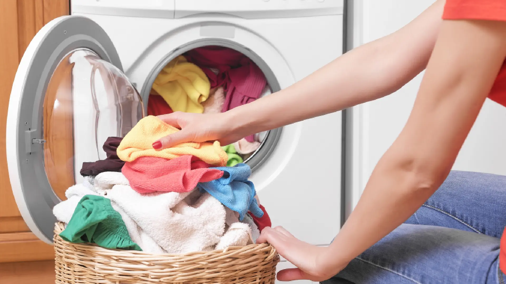 Mulher pegando roupas coloridas de cesto de roupa suja e colocando dentro da máquina de lavar