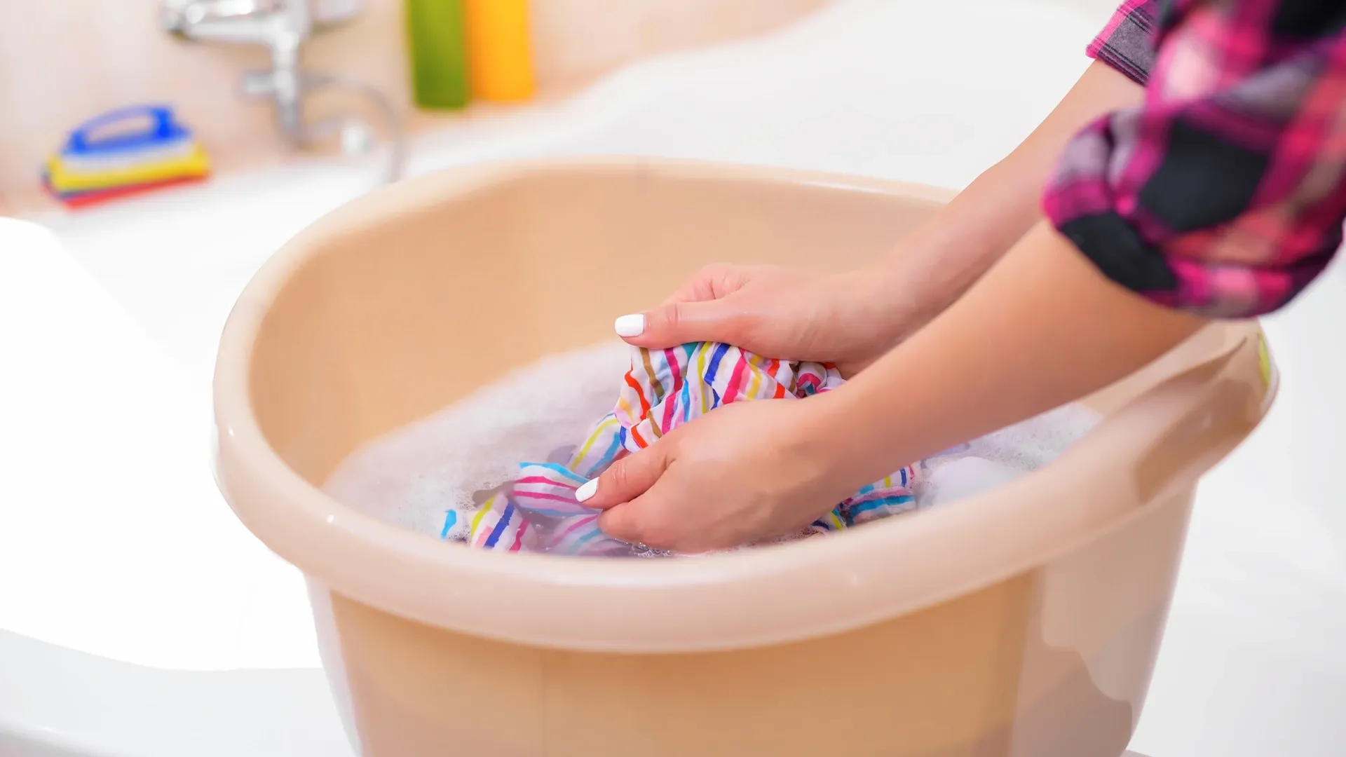 Mulher lavando roupa colorida à mão em uma bacia
