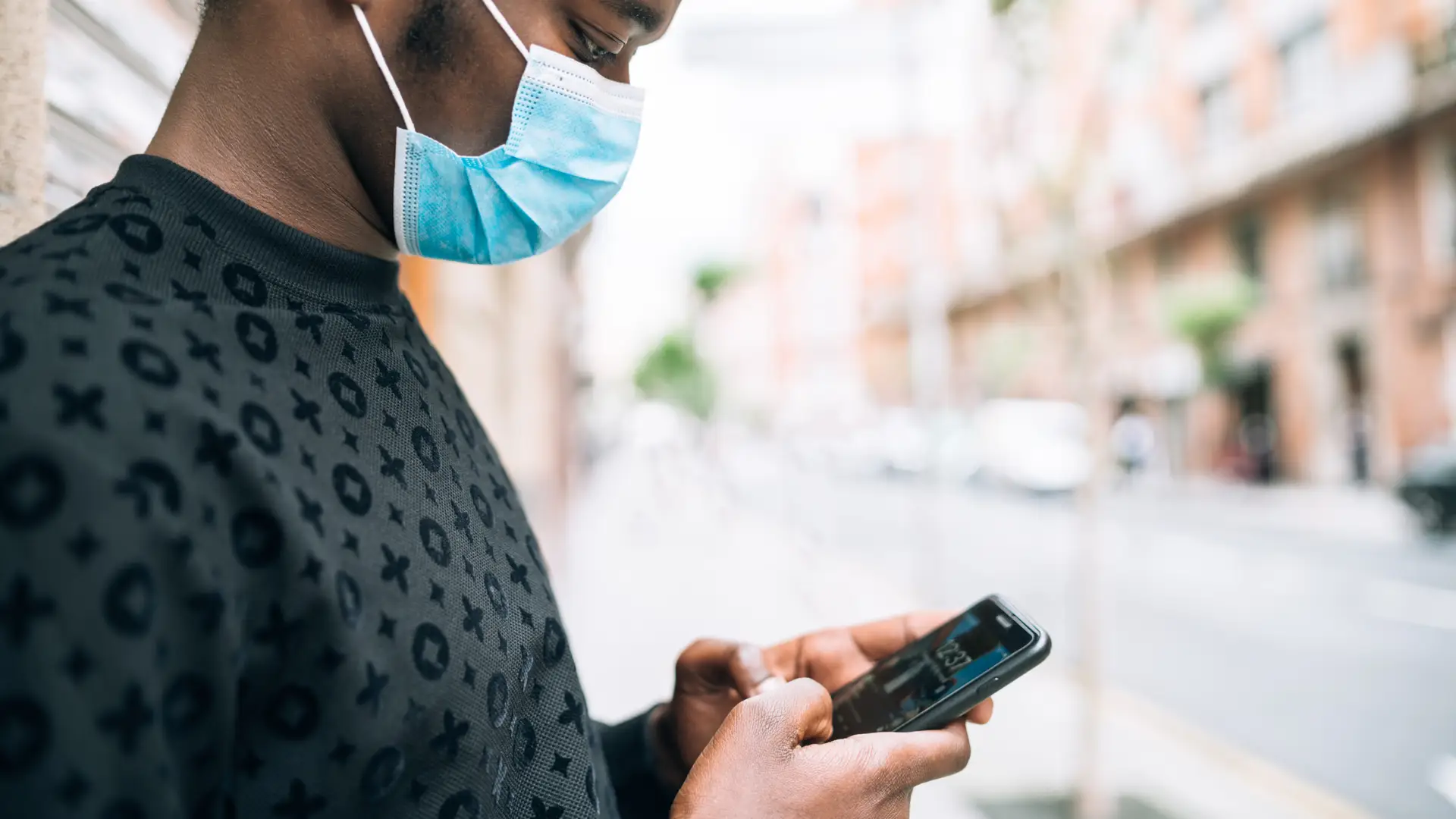 Homem negro de máscara segurando celular