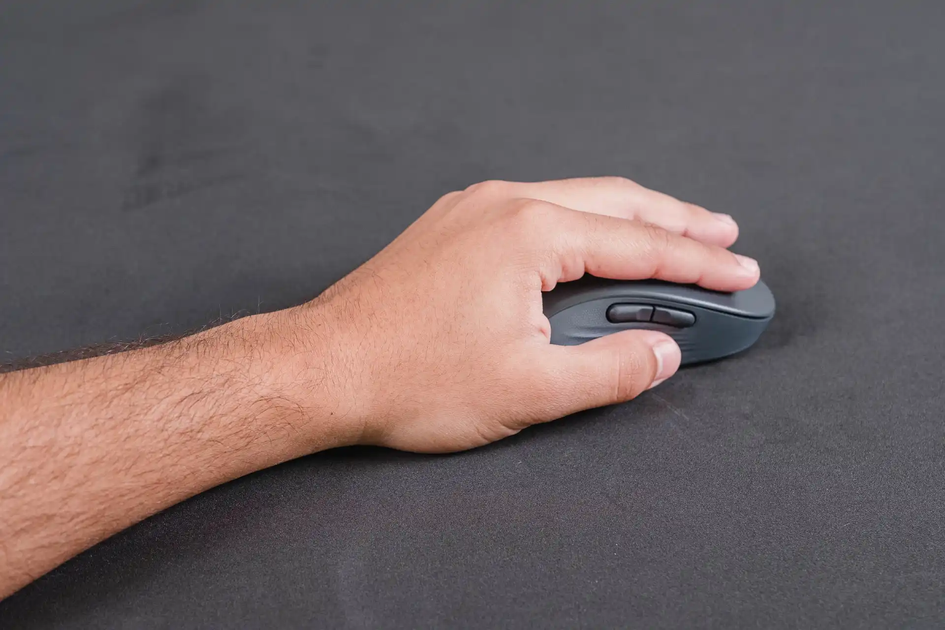 Mão esquerda segurando mouse Logitech M650L Left sobre mesa preta