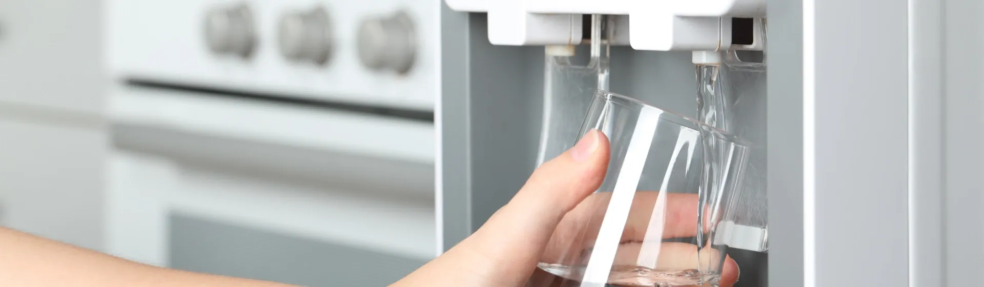 Mão segurando um copo de água, que está sendo enchido em um purificador de água