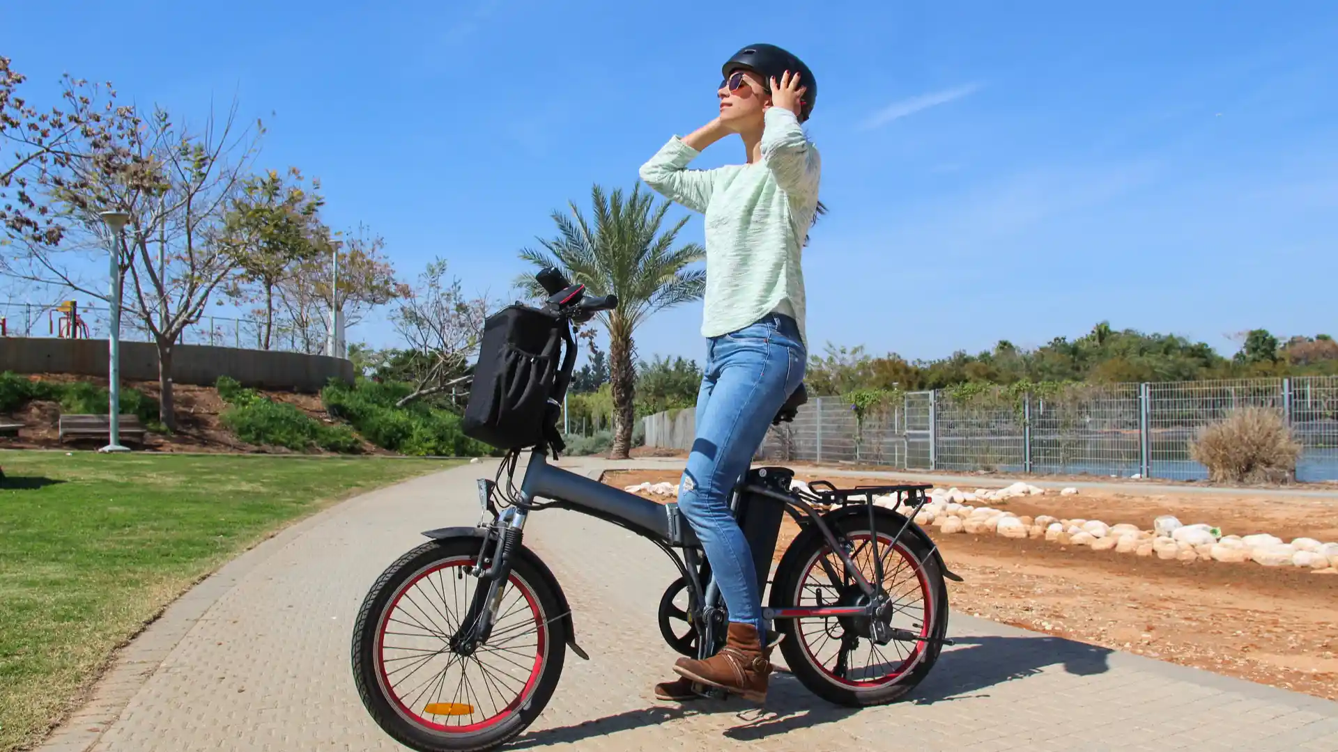 Mulher branca colocando capacete e usando bicicleta elétrica em um parque