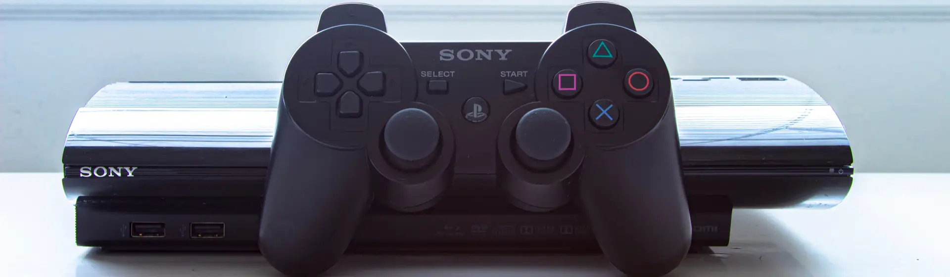 Um PS3 com controle, dispostos sobre uma mesa branca.