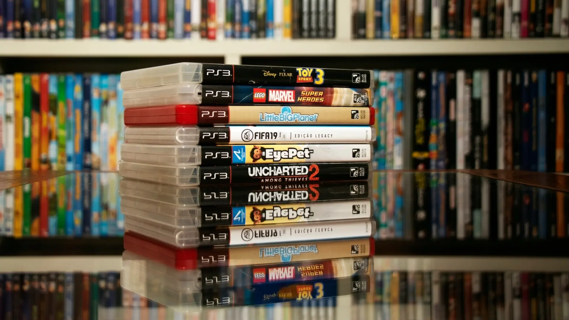 Diversos jogos de PS3 expostos sobre uma mesa de vidro.
