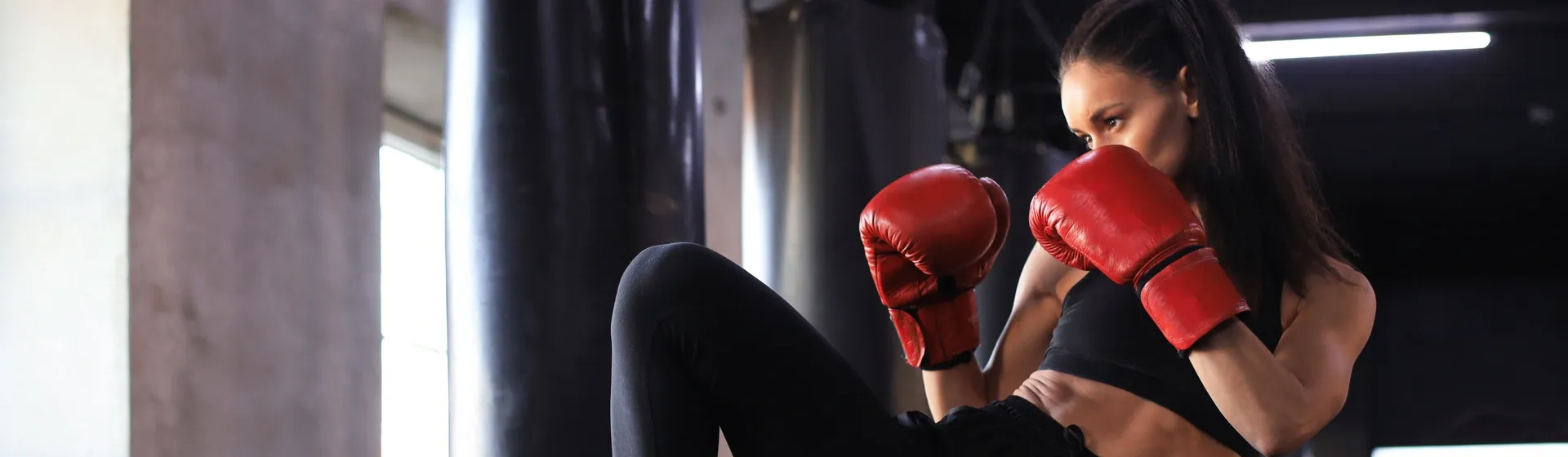 Mulher, com luvas de Muay Thai vermelhas, faz posição de defesa durante treino