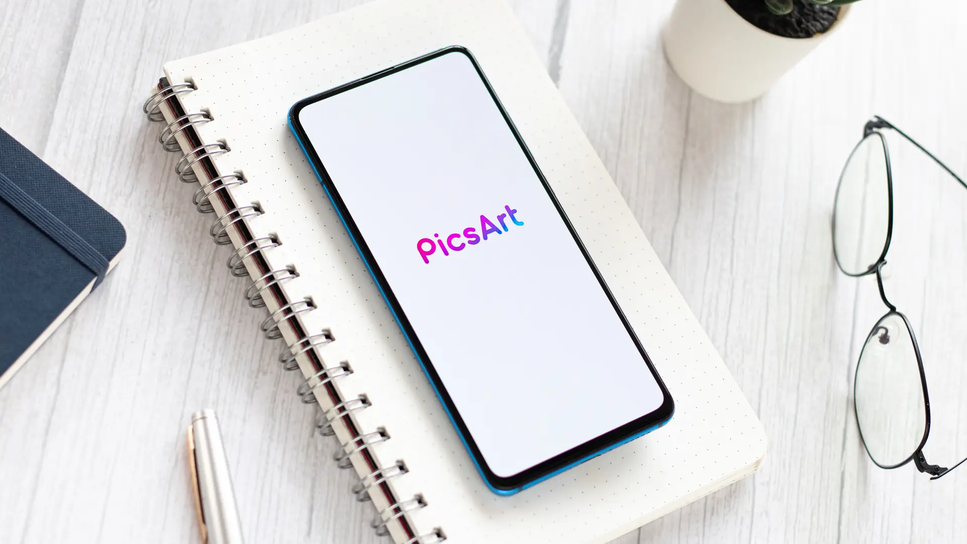 Celular com o app PicsArt sobre caderno ao lado de óculos