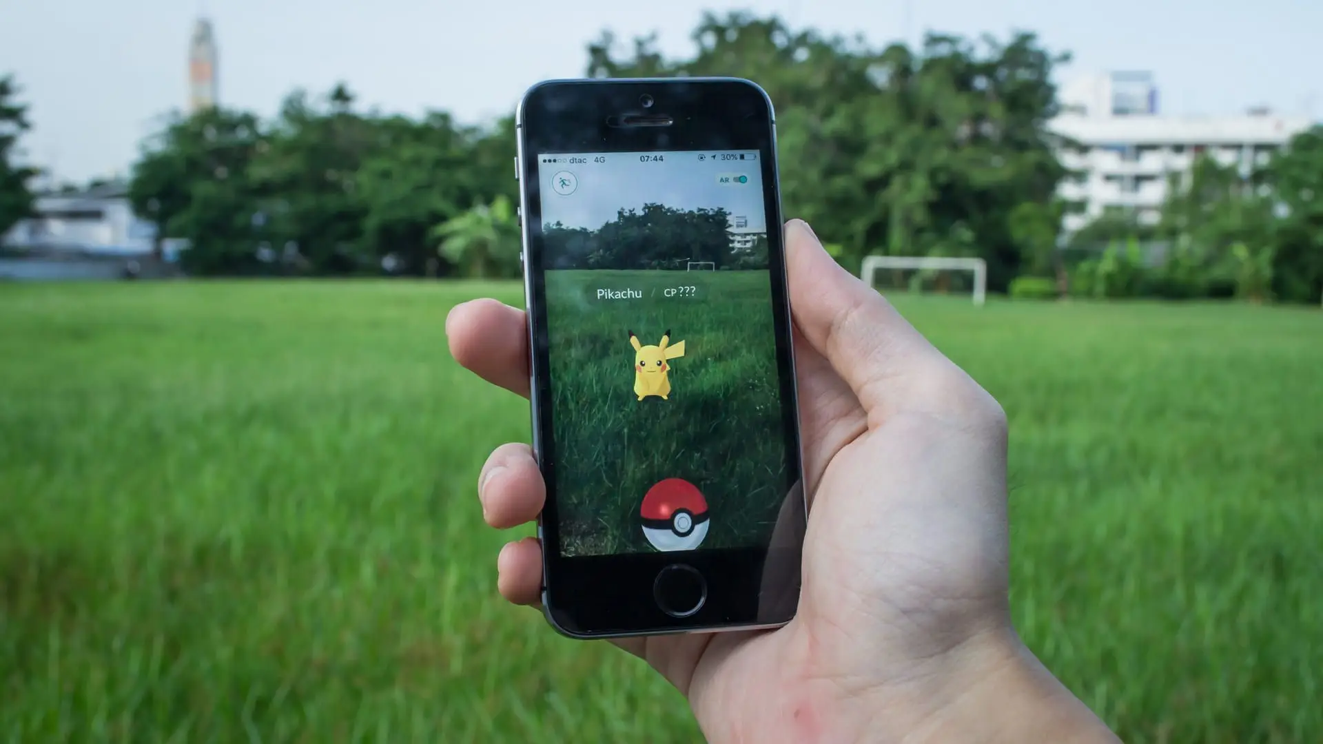 Uma pessoa segura um celular enquanto joga Pokémon Go em um campo com grama