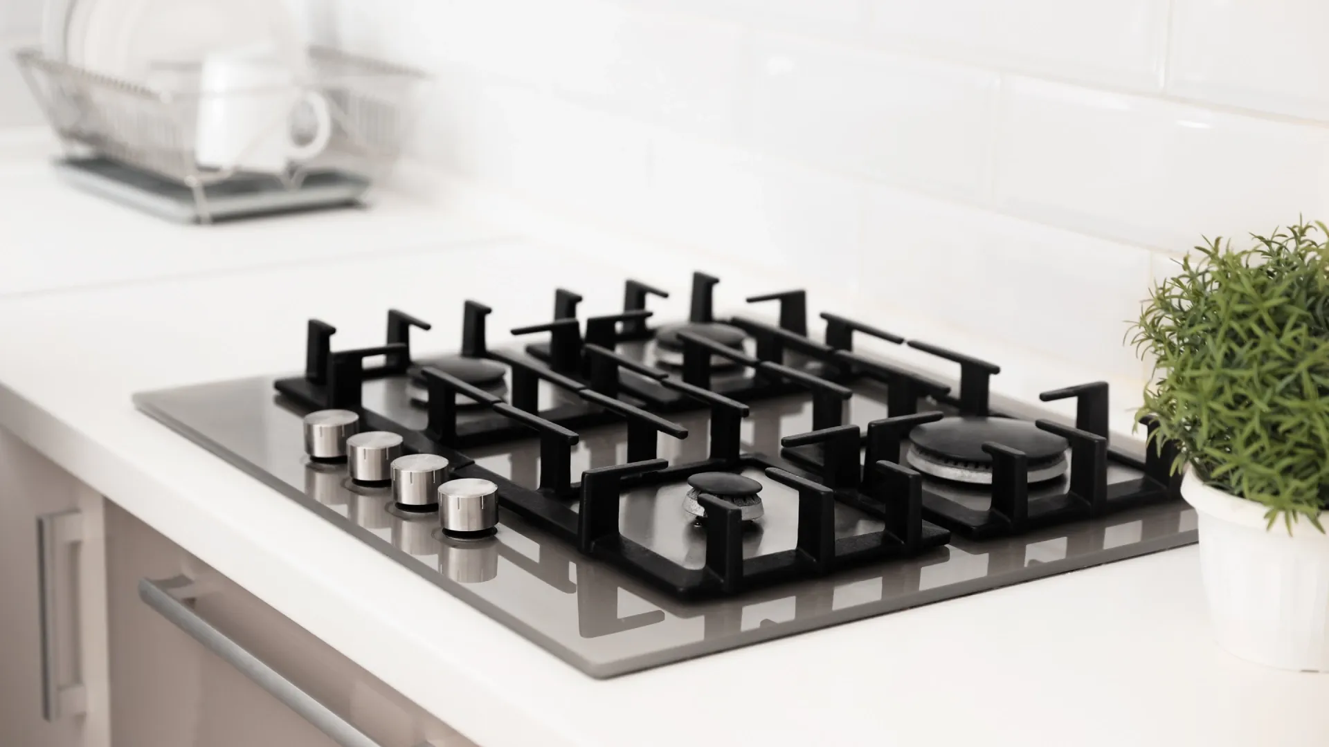 Fogão cooktop 4 bocas preto com cinza, instalado em uma bancada de cozinha branca