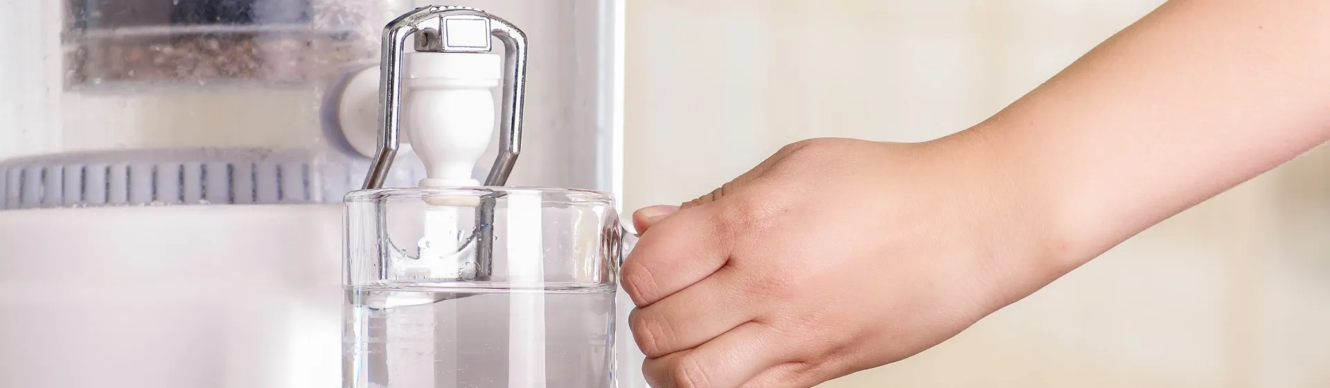Mão branca segurando um copo de água cheio no filtro de água
