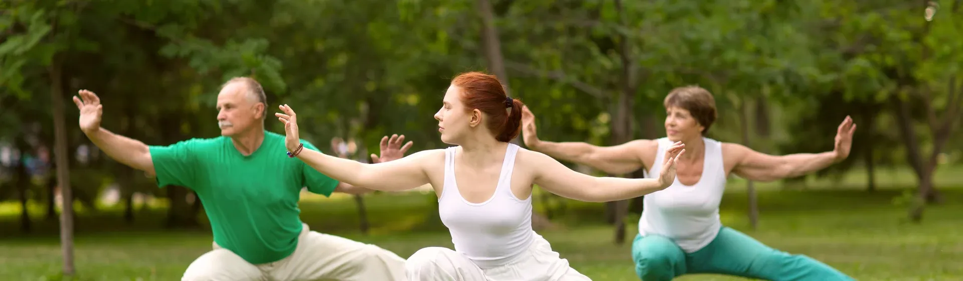 Três pessoas fazem movimento com os braços do Tai Chi Chuan em um parque