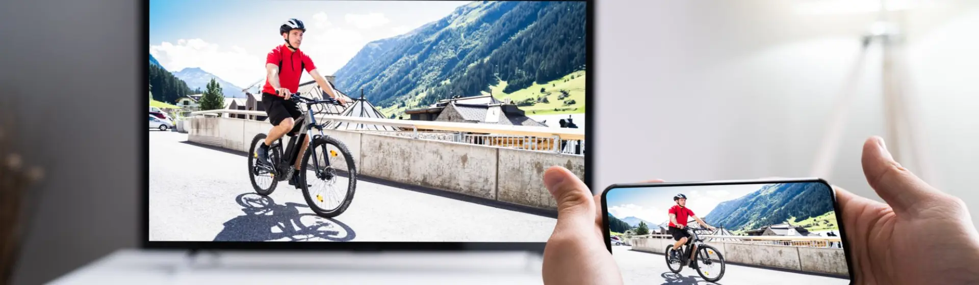Mão de pessoa segurando smartphone e fazendo processo de espelhar celular na TV com imagem de homem andando de bicicleta 