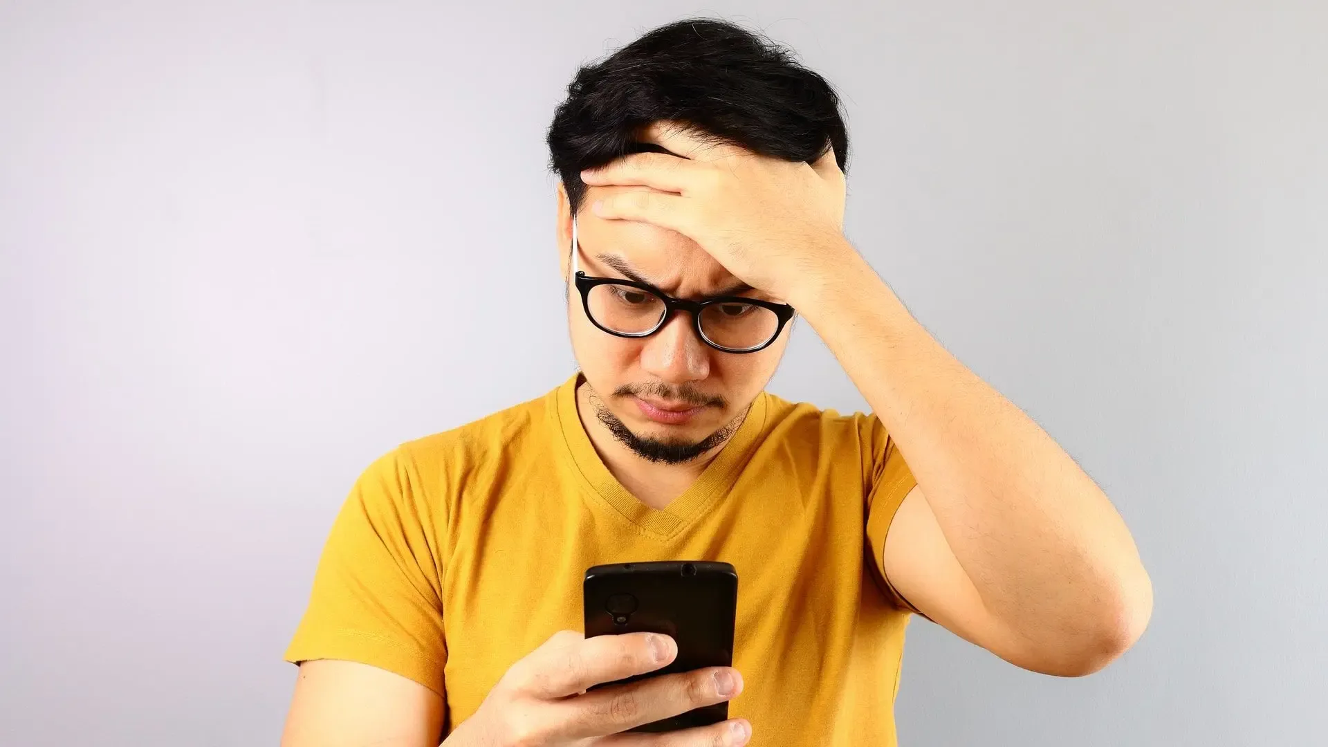 Homem com a mão na cabeça e aparência de preocupado mexendo no celular