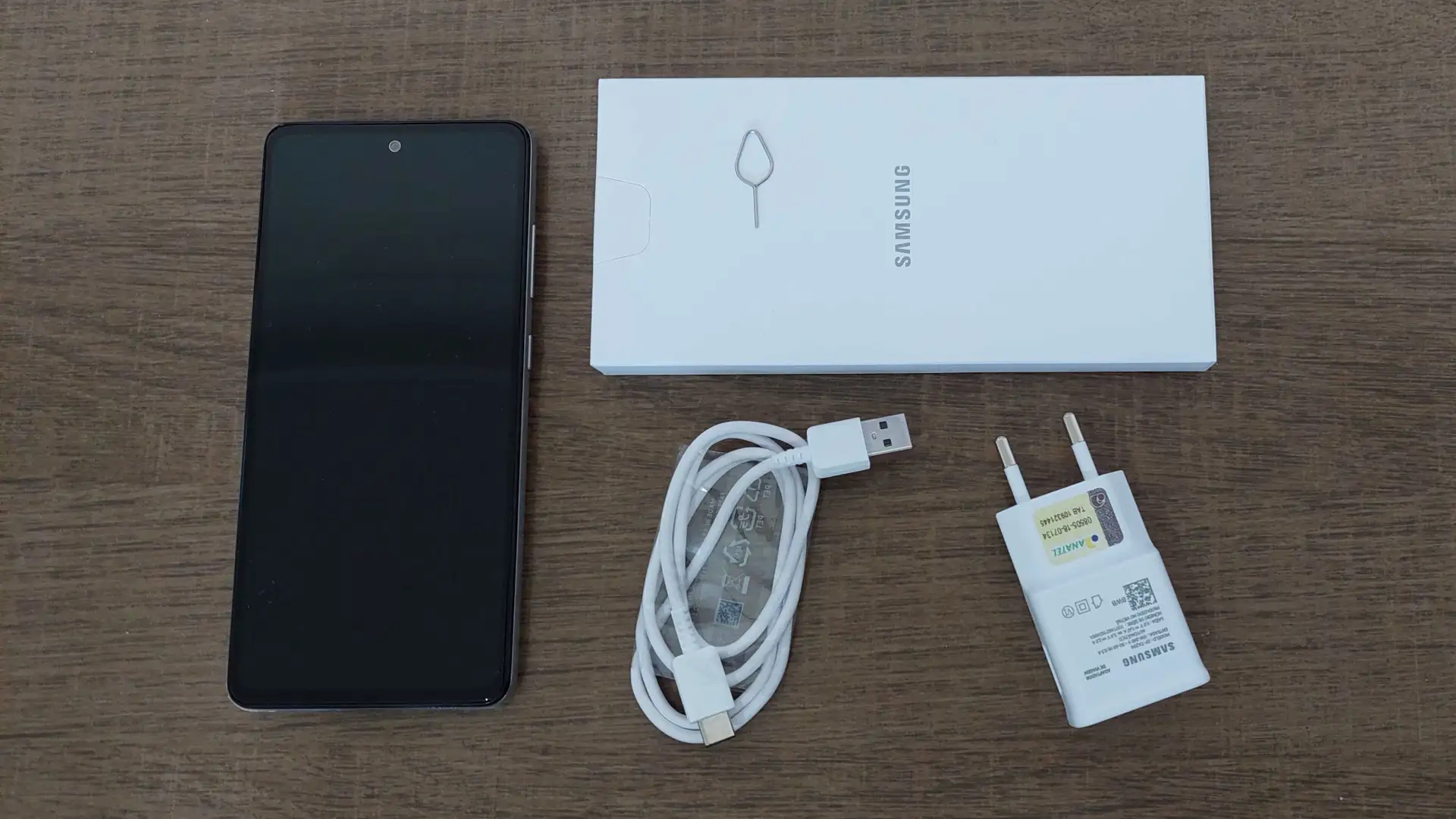 Foto dos itens que vem na caixa do Galaxy A52s 5G dispostos em cima de uma mesa de madeira