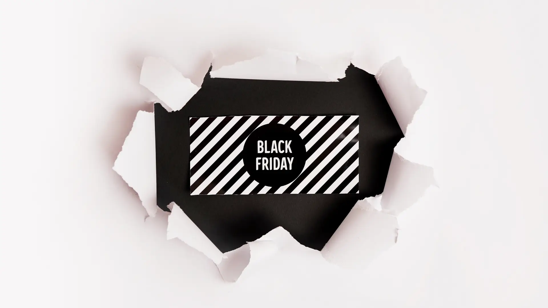 Um fundo branco sendo partido para revelar no meio o logo da Black Friday sobre um fundo preto e listrado. 