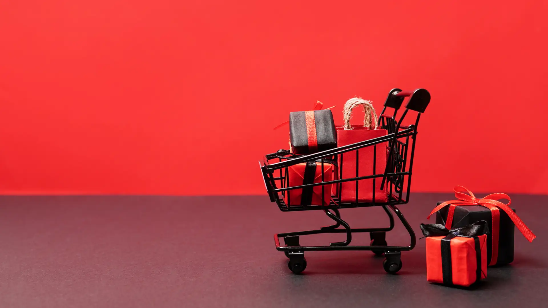 Um carrinho de compras com embrulhos pretos e vermelhos sobre um fundo vermelho. 
