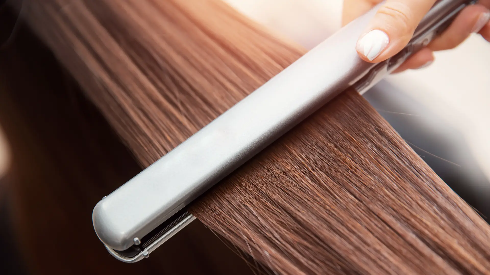 Chapinha prateada sendo passada em mecha de cabelo castanho claro