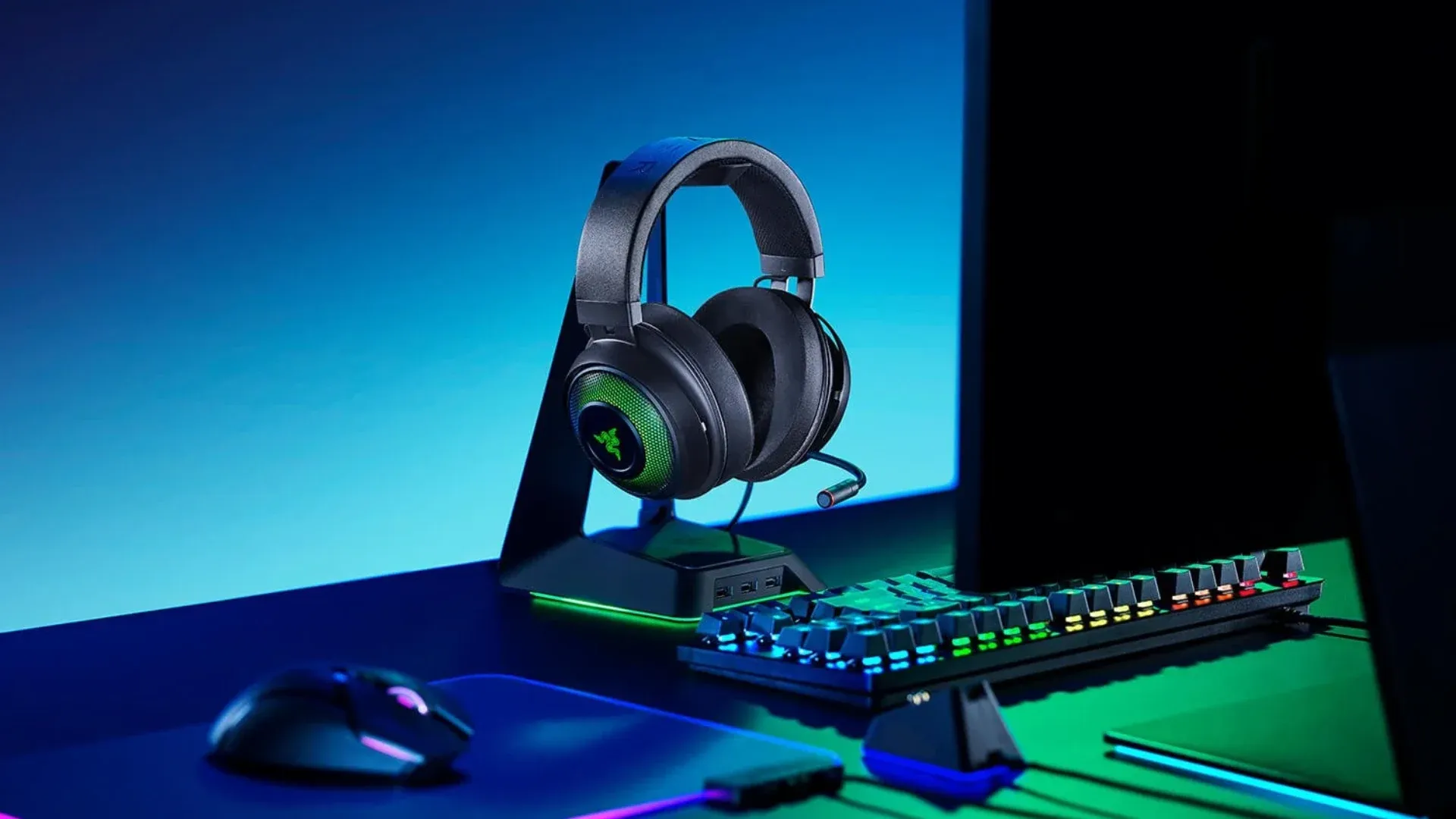 A imagem apresenta um headset Razer Kraken disposto sobre um suporte, em cima de uma mesa com diversos outros produtos da Razer.