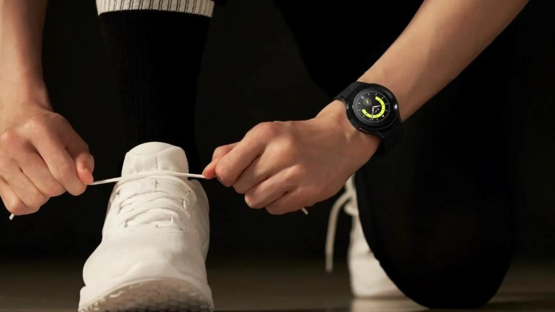 Duas mãos, sendo uma delas com o relógio Galaxy Watch 5 Pro no pulso, amarram tênis branco